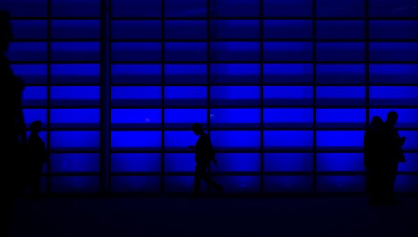 Silhouettes of people walking and using phones against a blue illuminated wall.