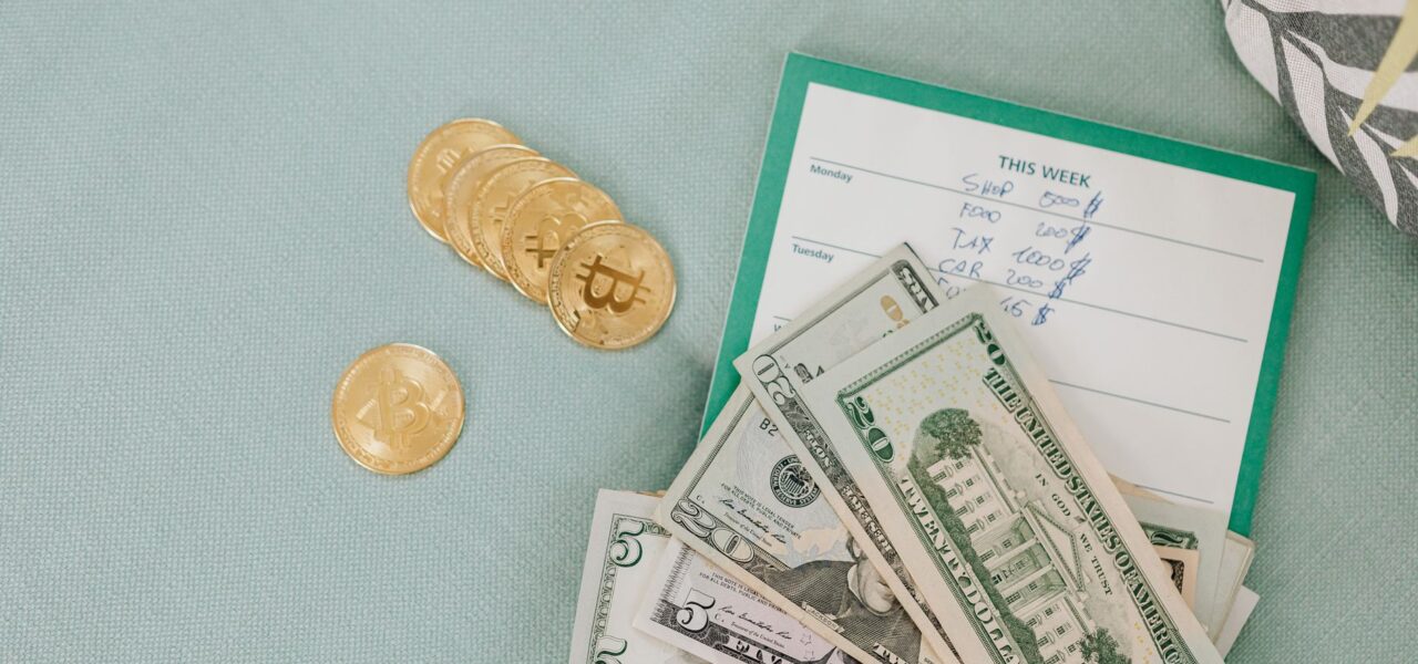 Close-up of U.S. dollars and Bitcoin coins placed on a weekly budget planner, symbolizing modern finance.